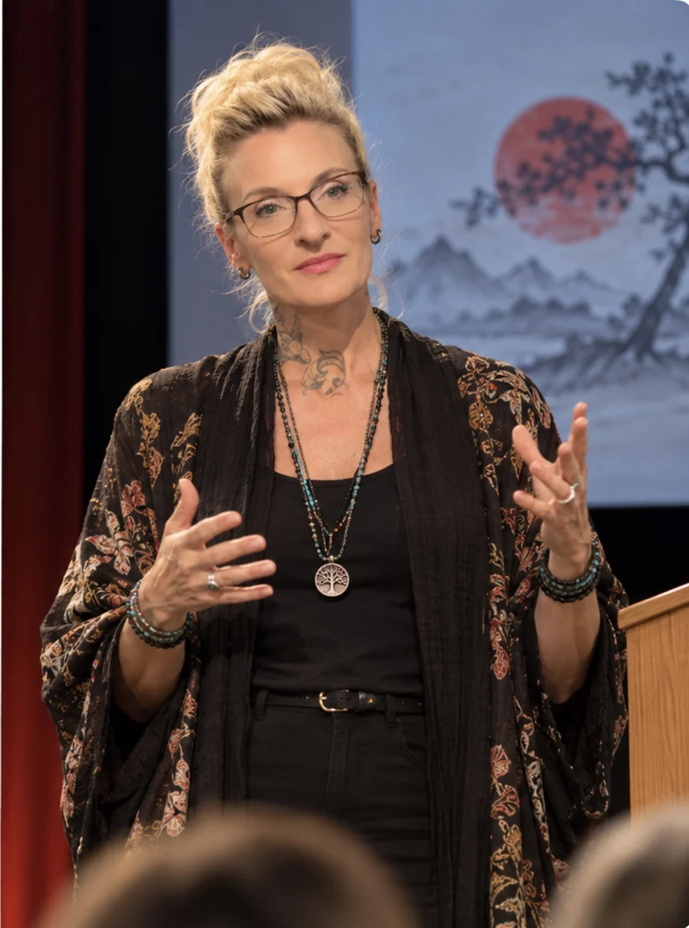 Leslie Brewer presenting with expressive hand gestures beside a lectern and sumi-e backdrop.